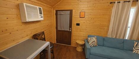 A cozy cabin interior with a wooden ceiling, a table, a sofa, and a window.