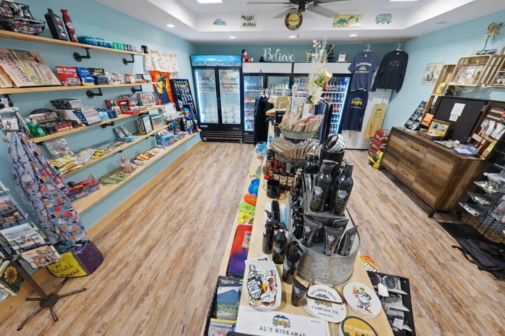 A retail store with shelves stocked with various items, a display counter with products, and a sign that reads 'Believe'.