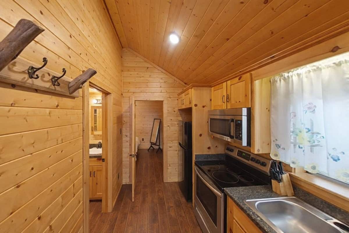 A wooden interior with a kitchen area, including a microwave, stove, and sink.