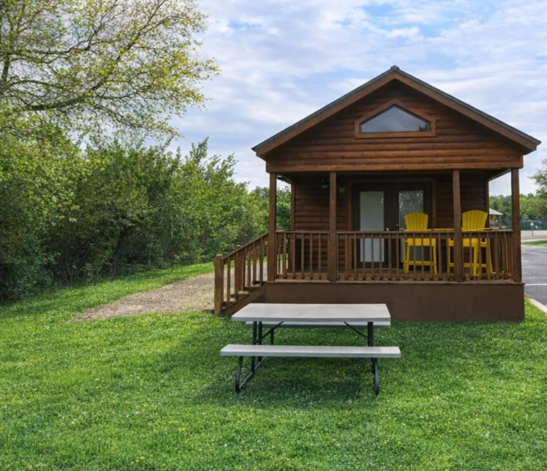A wooden cabin with a porch, a picnic table, and two chairs.