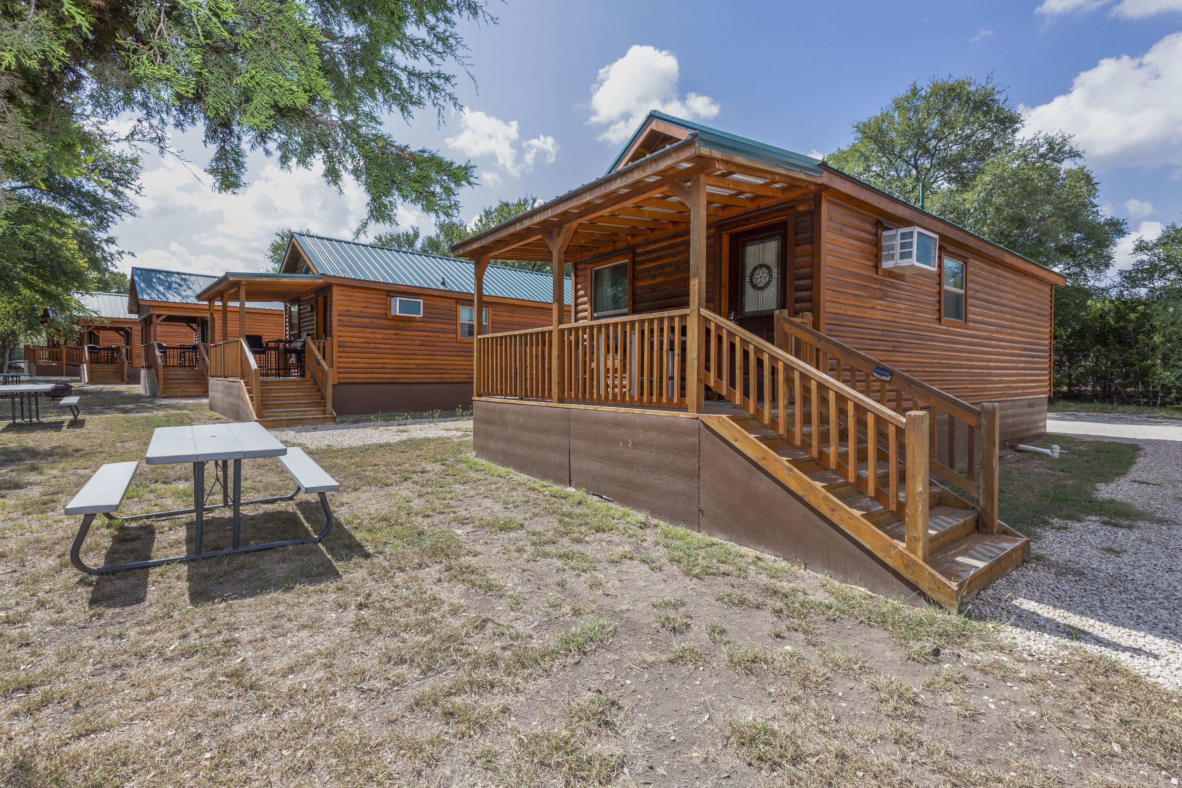 A wooden cabin with a porch, a picnic table, and a staircase leading to the entrance.