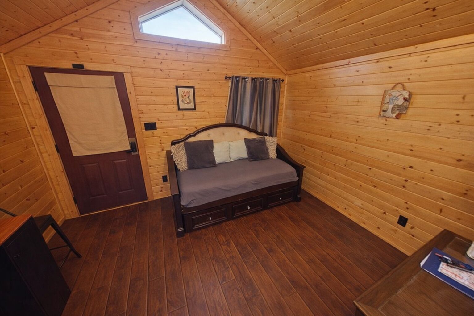Een knus houten slaapkamer met een bed, een deur, een klein tafeltje en een raam.