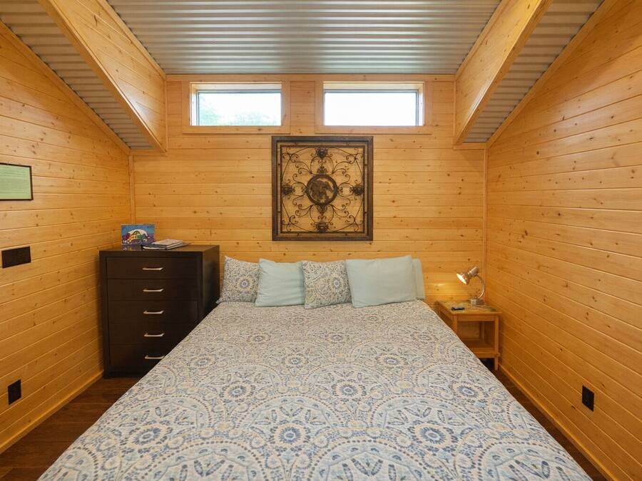 Camera da letto in una baita di legno, con un letto, una cassettiera, due finestre e un'opera d'arte appesa al muro.