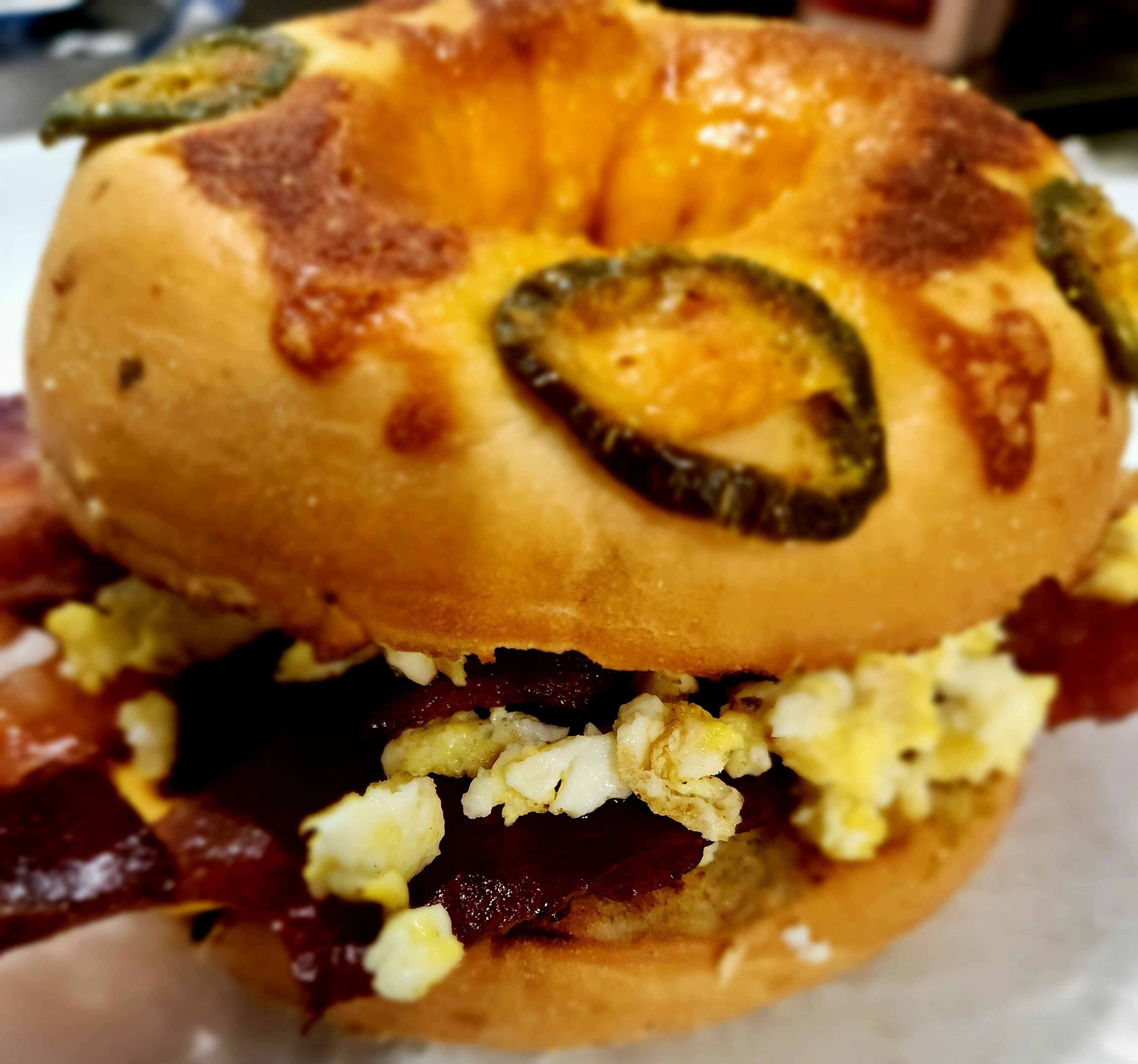 A close-up of a breakfast sandwich with a toasted bun, eggs, bacon, and a slice of cheese.
