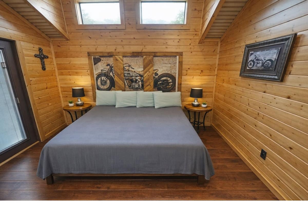A wooden-paneled bedroom with a bed, two nightstands, a cross, and a motorcycle-themed artwork on the wall.