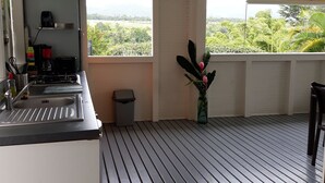 A kitchen with a sink, stove, and a window overlooking greenery. - CITRONELLA APARTMENT (PETIT-BOURG)