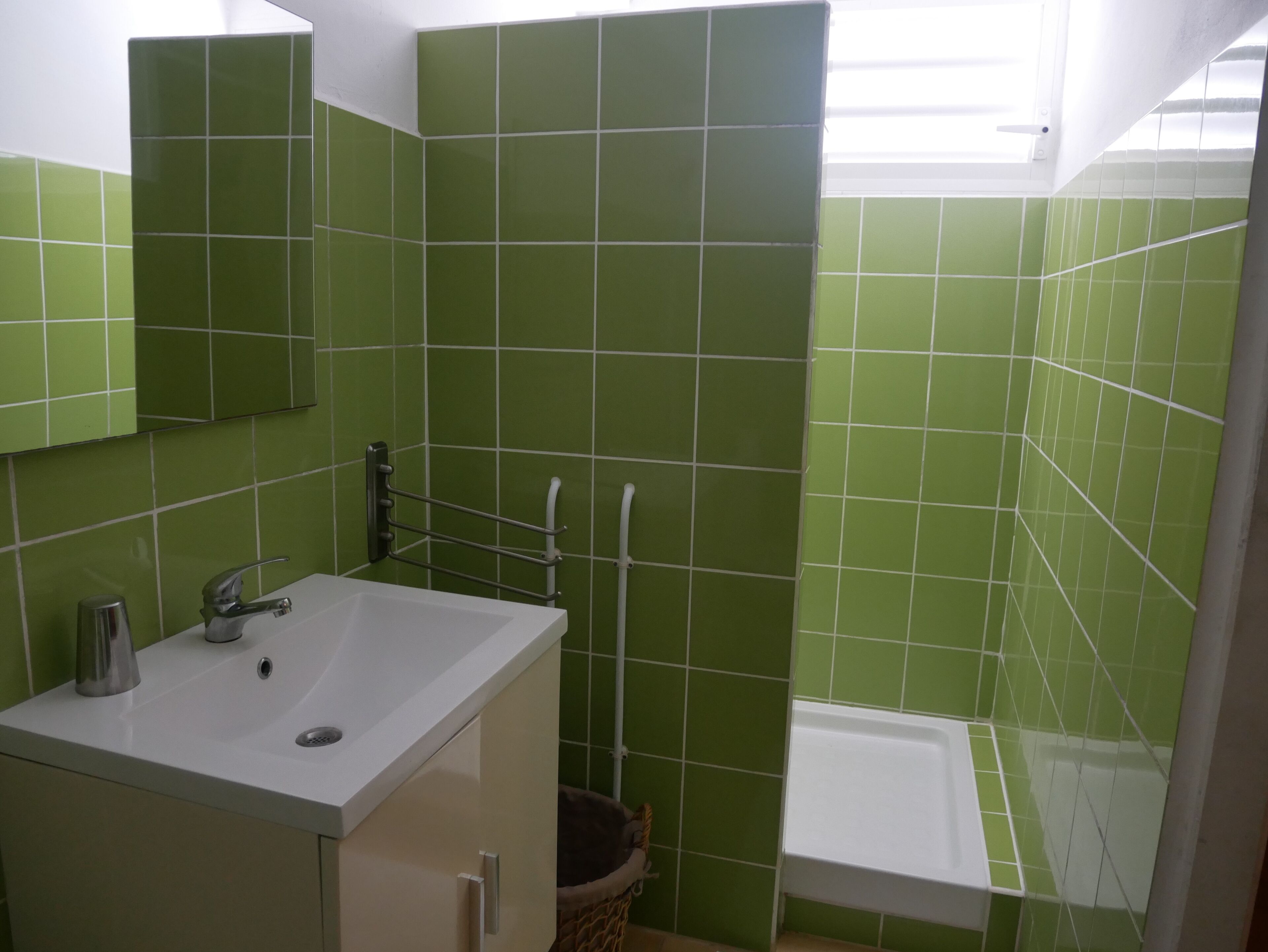 Un baño con azulejos verdes, un lavamanos blanco, un espejo y una zona de ducha.