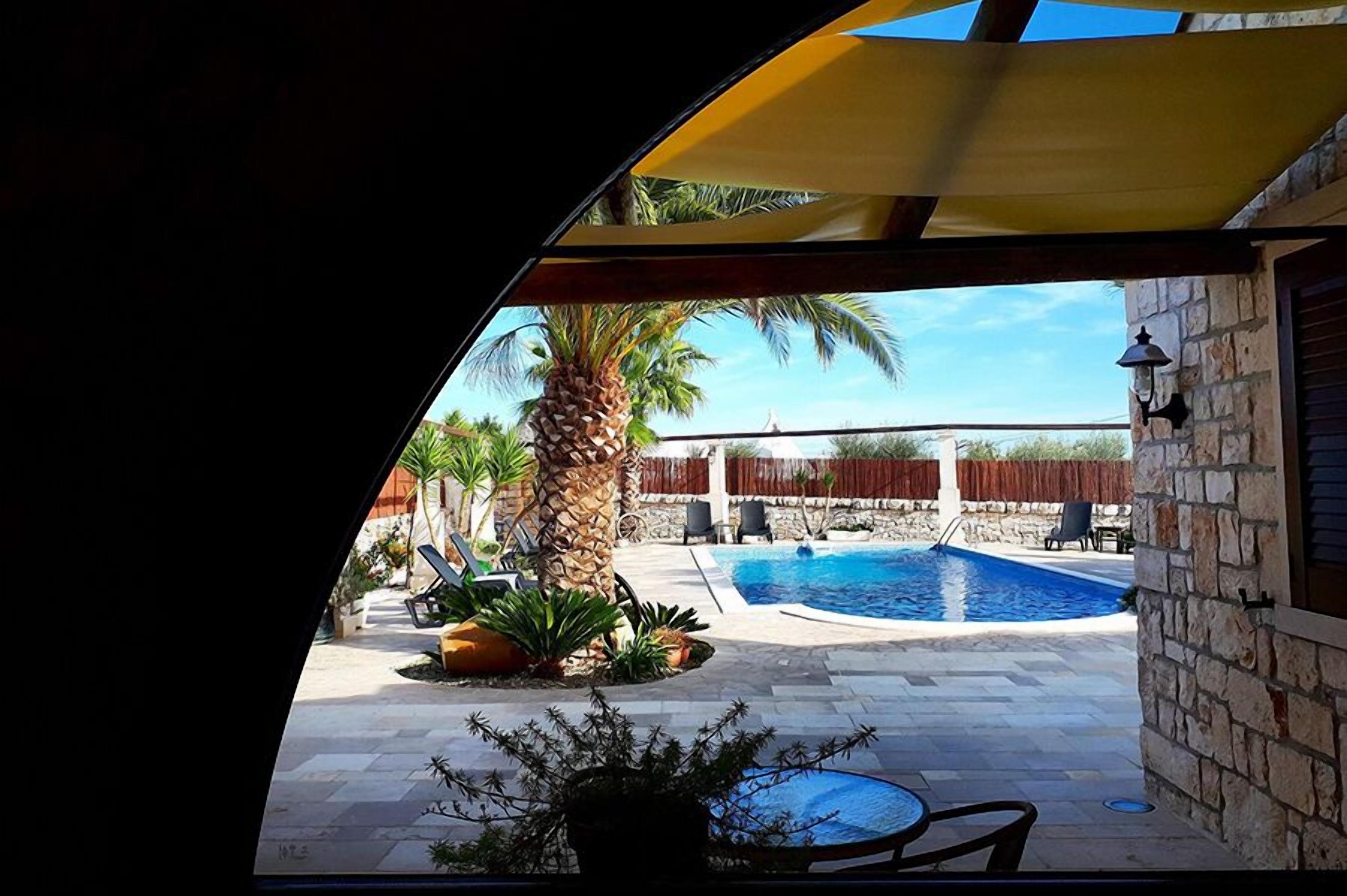 A pool area with a stone wall, palm trees, and outdoor furniture.