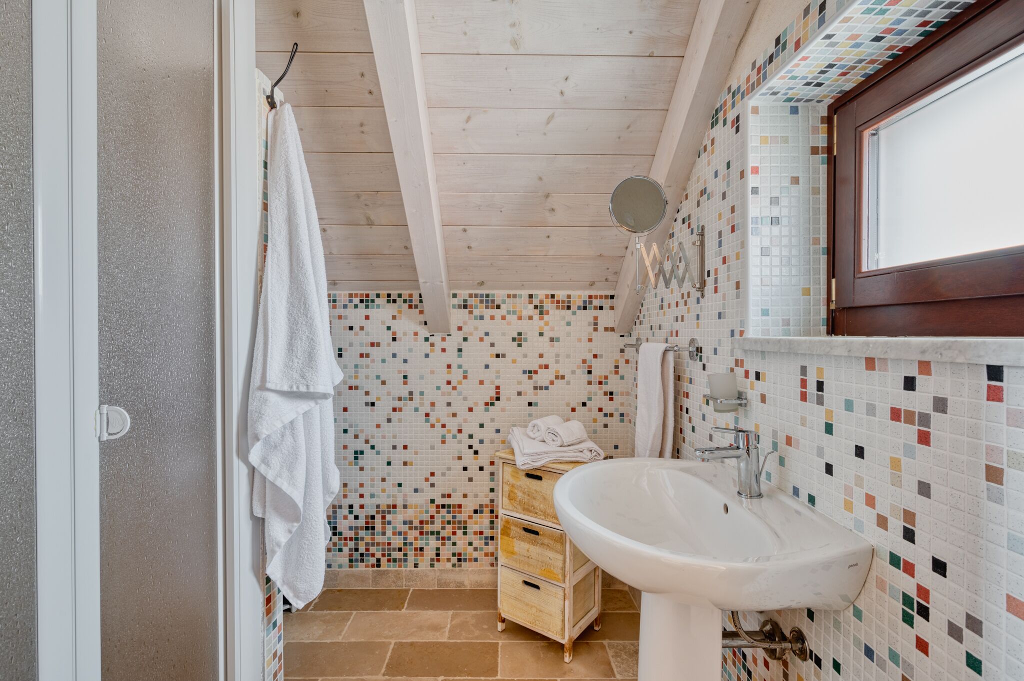 A bathroom with a wooden ceiling, a tiled mosaic wall, a white sink, and a wooden cabinet.