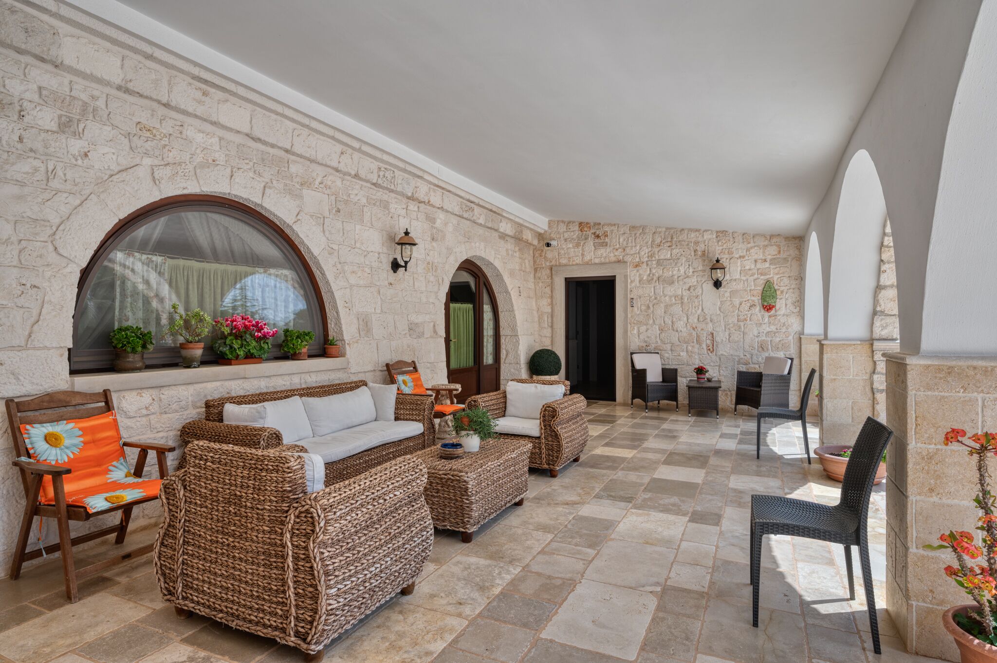 A covered outdoor seating area with wicker furniture, stone walls, and potted plants.