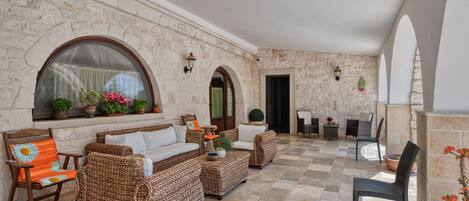A covered outdoor seating area with wicker furniture, stone walls, and potted plants.