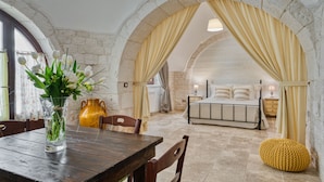 A rustic interior with stone arches, a wooden dining table, and a bed with a white headboard. - Trulli D'Autore (Martina Franca)