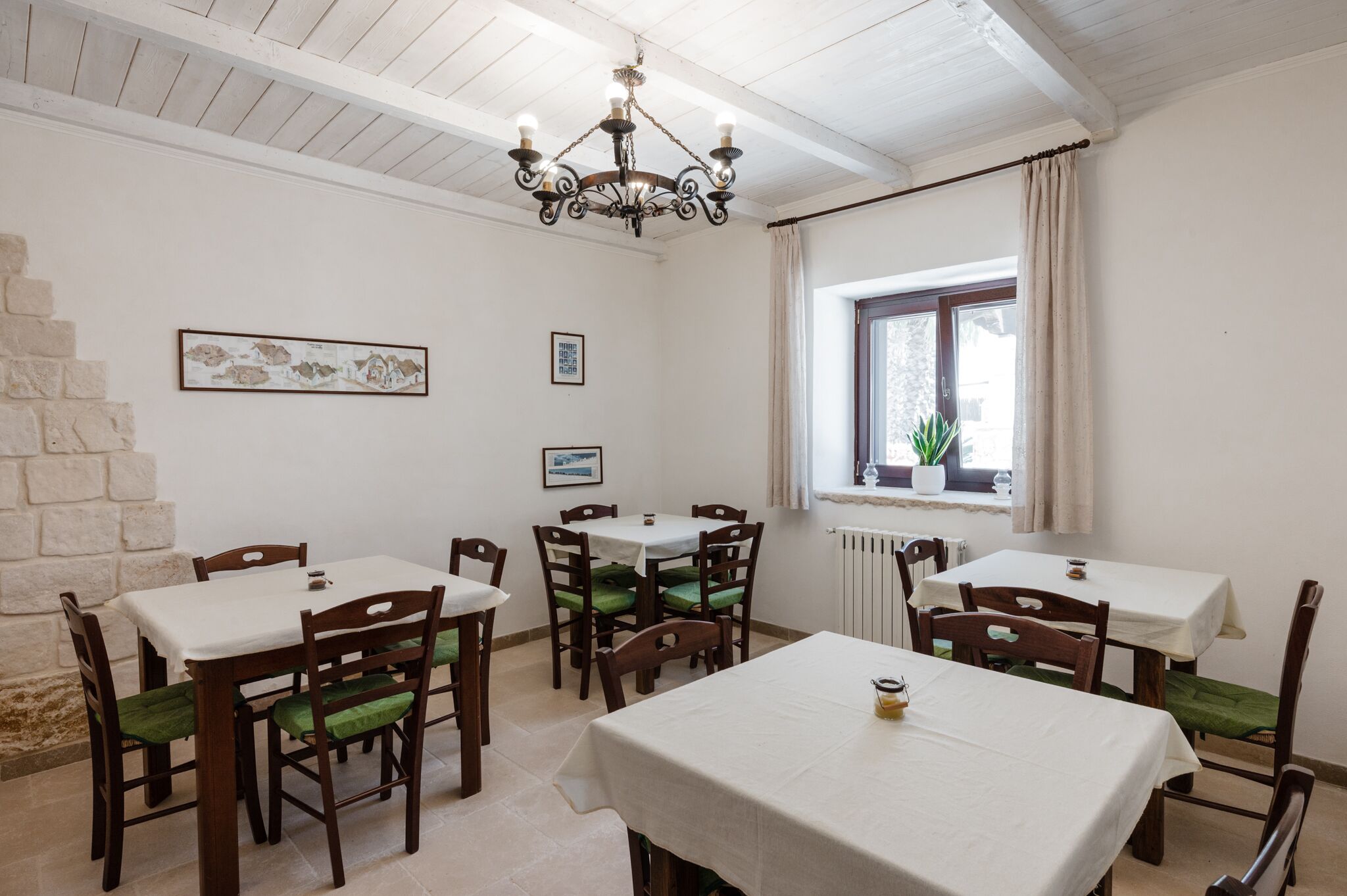 Un comedor con mesas y sillas de madera, una araña y una ventana con cortinas.