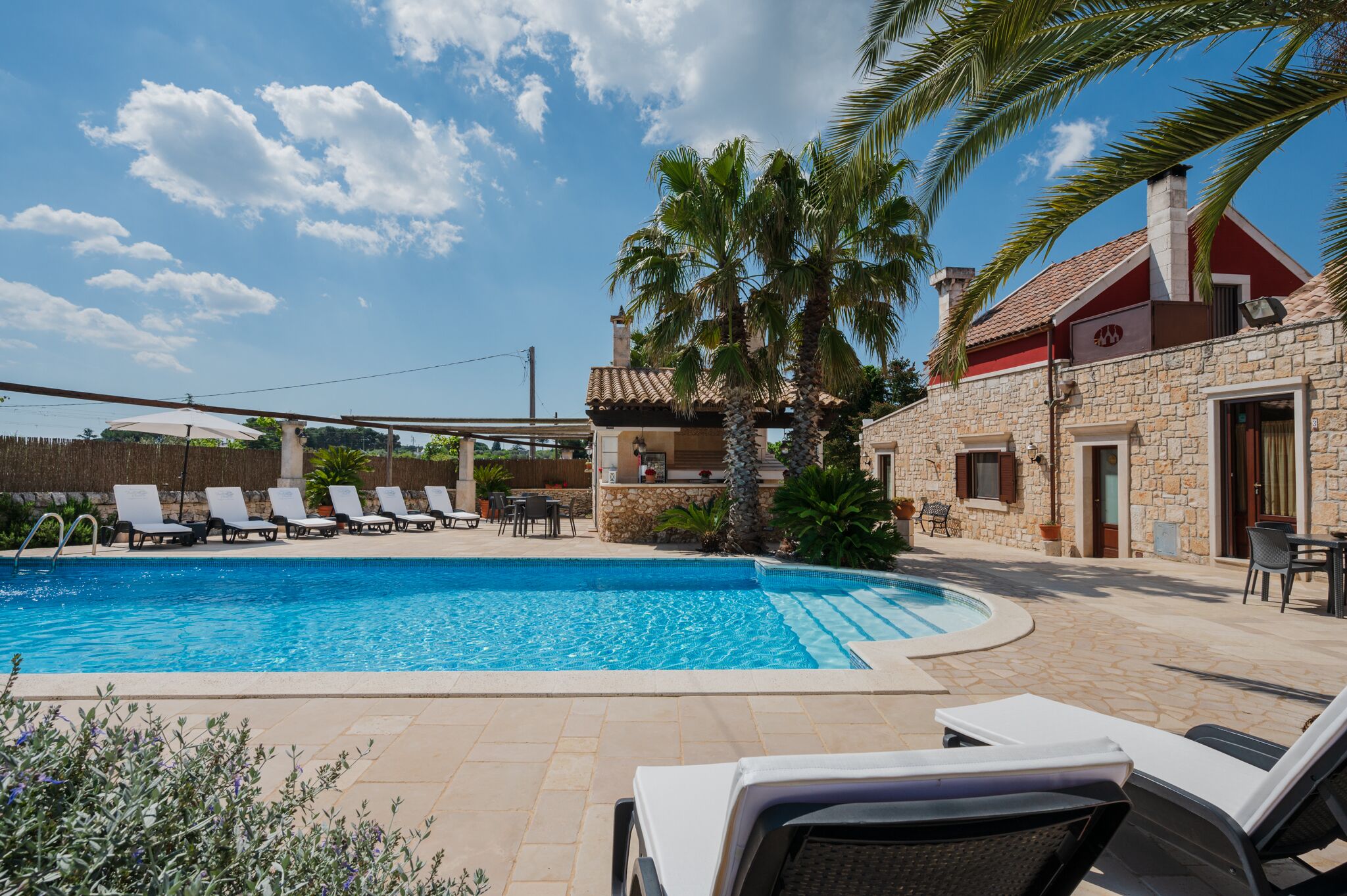 A pool area with lounge chairs, a stone building, and palm trees.