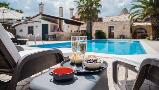A poolside table with a tray of food and drinks, overlooking a swimming pool with a stone building in the background. - Trulli D'Autore (Martina Franca)