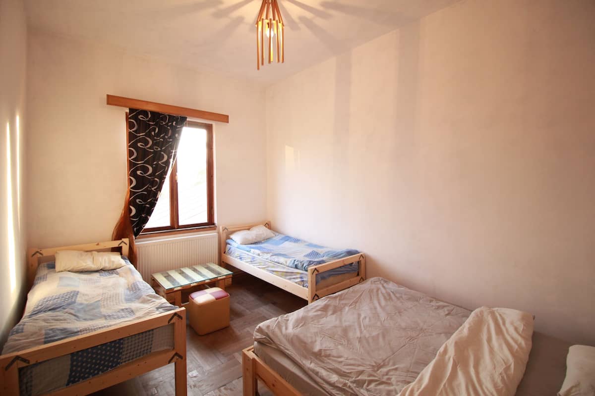 Une chambre avec deux lits simples, une petite table et une fenêtre avec des rideaux.