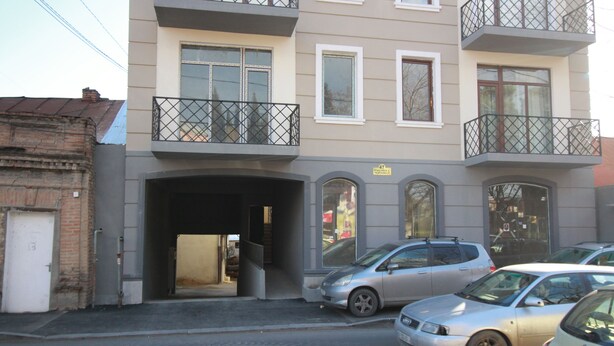 Un immeuble à plusieurs étages avec une entrée de garage, des voitures garées et un balcon.