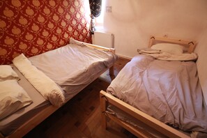 Duas camas de solteiro num quarto com papel de parede estampado e radiador.