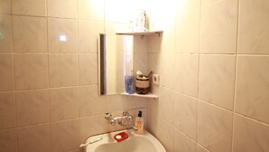 Une salle de bain avec un lavabo blanc, un miroir et une étagère contenant des articles de toilette.