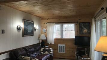 A cozy living room with a leather sofa, a television, and a window with curtains.