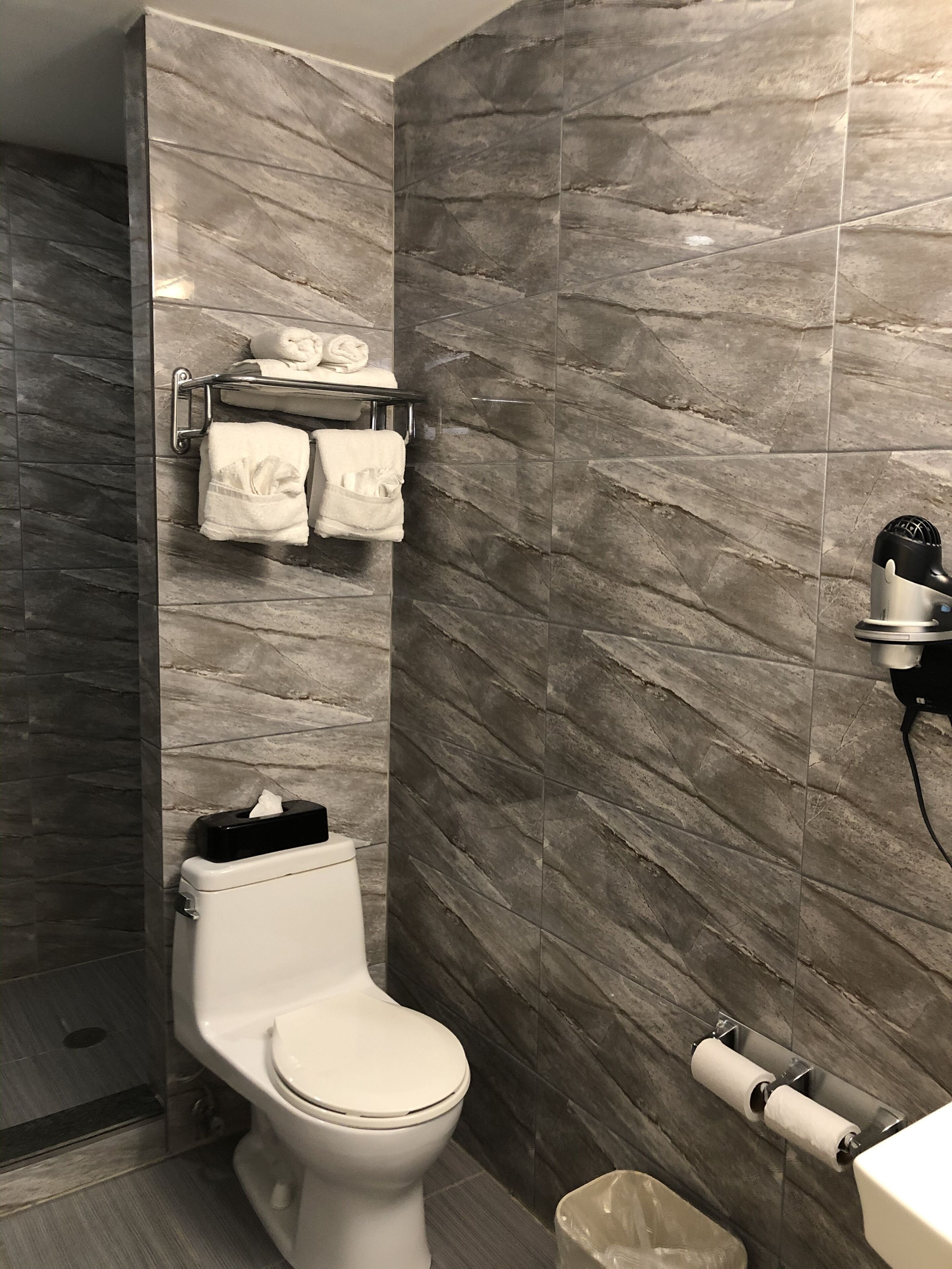 A modern bathroom with a marble wall, a toilet, a towel rack with towels, and a hairdryer.