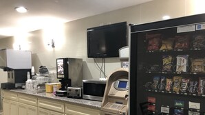 Una cocina con cafetera, microondas, tostadora, refrigerador lleno de refrigerios y una máquina expendedora.