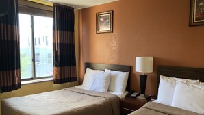 Habitación de hotel con dos camas, una mesita de noche con lámpara, un cuadro enmarcado en la pared y una ventana con cortinas.
