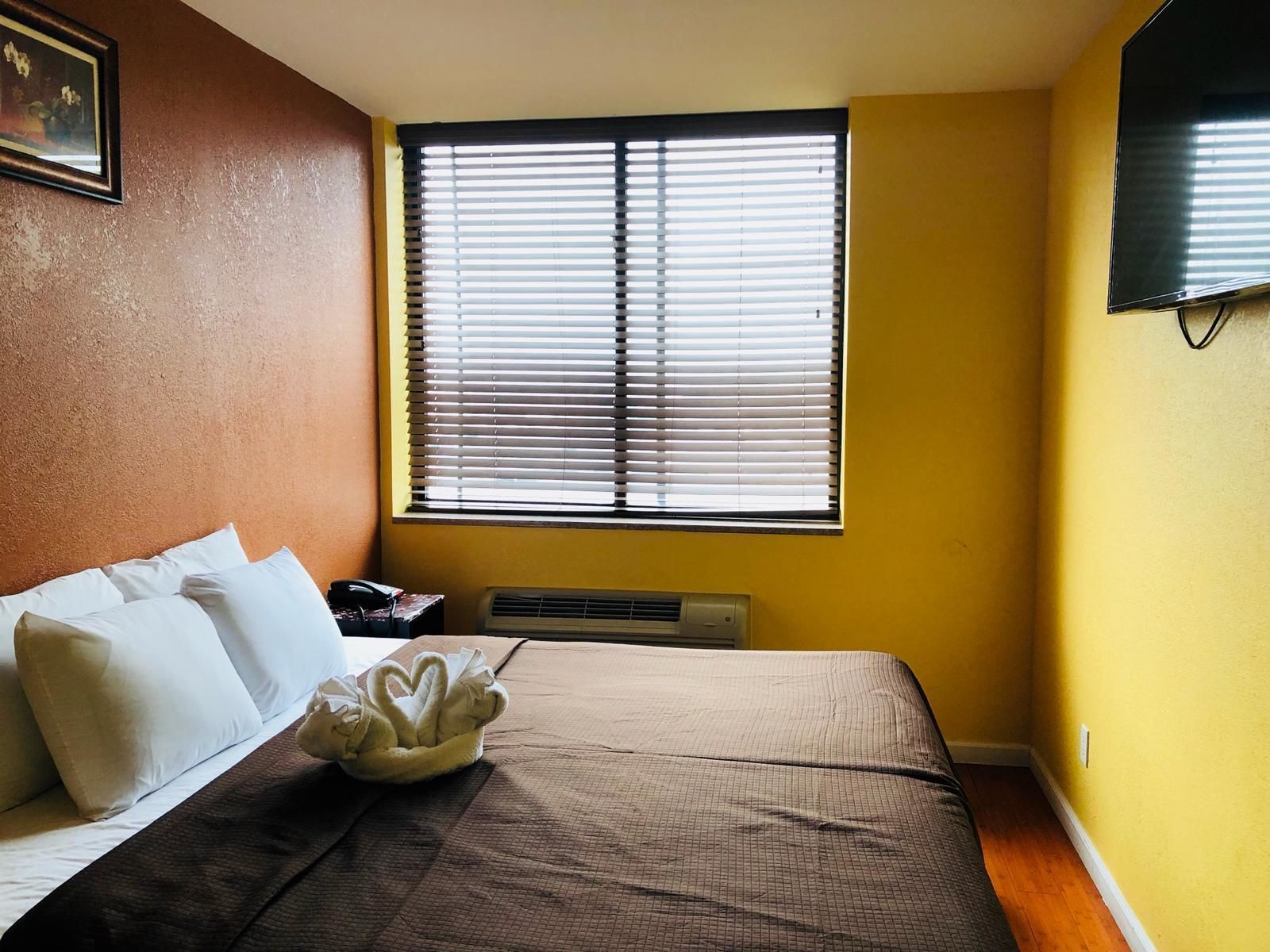 Habitación de hotel con cama, almohadas, un adorno con forma de cisne, una mesita de noche con teléfono y una ventana con persianas.