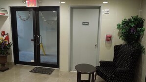 Un vestíbulo con mostrador de recepción, puerta de cuarto de almacenamiento y una zona de estar con una silla y una pequeña mesa.