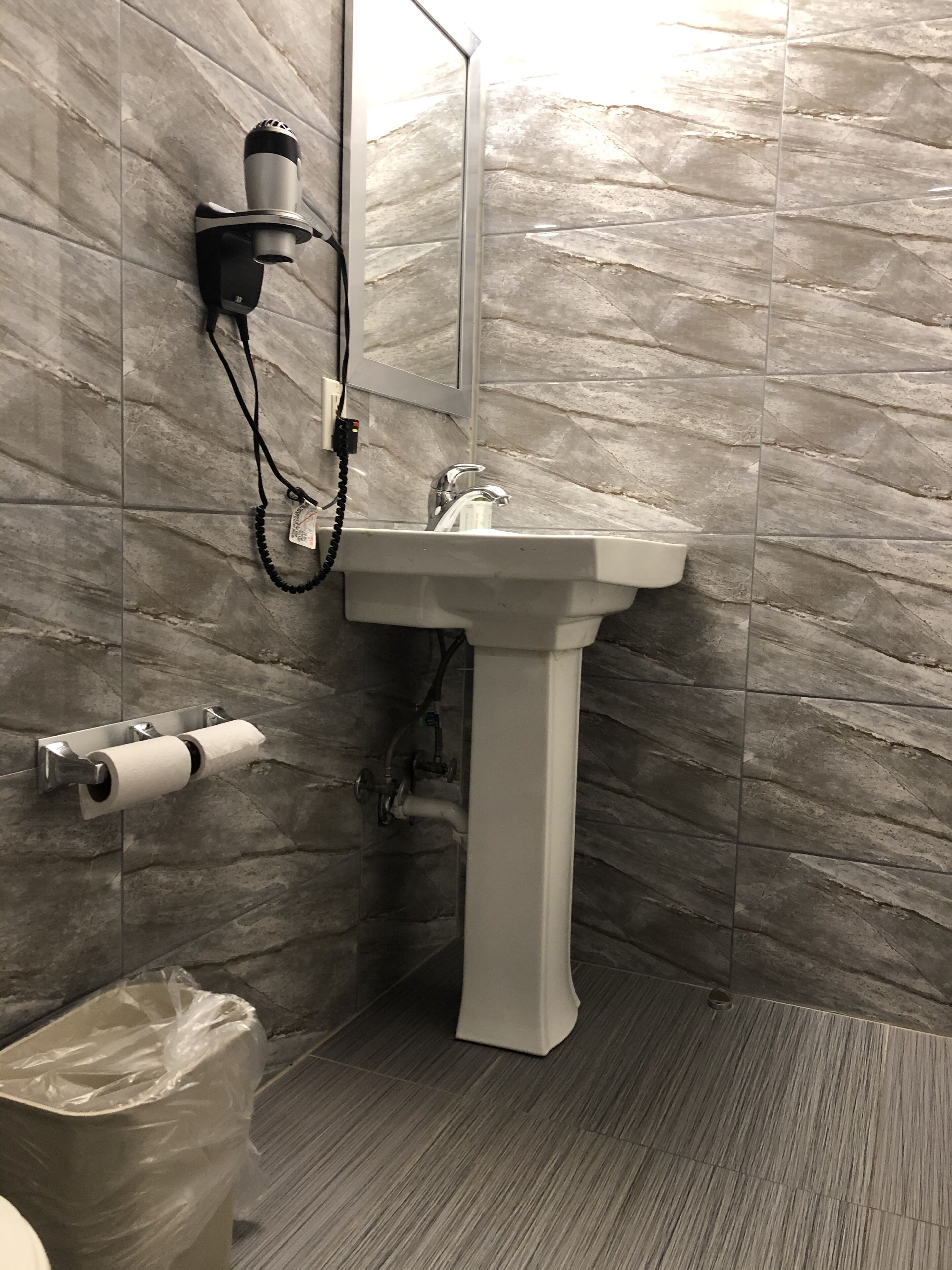 Ein Badezimmer mit einem weißen Waschtisch, einem Handtuchspender, einem Toilettenpapierhalter und einem Mülleimer.