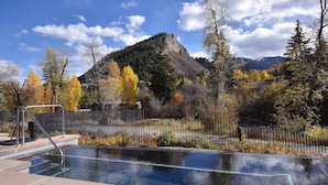 A swimming pool with a mountain backdrop, surrounded by trees and a fence. - Charlie's Slopeside: Gondola Access, Private Patio, Resort Amenities, BC Views, Ski Valet + Pool (Avon)