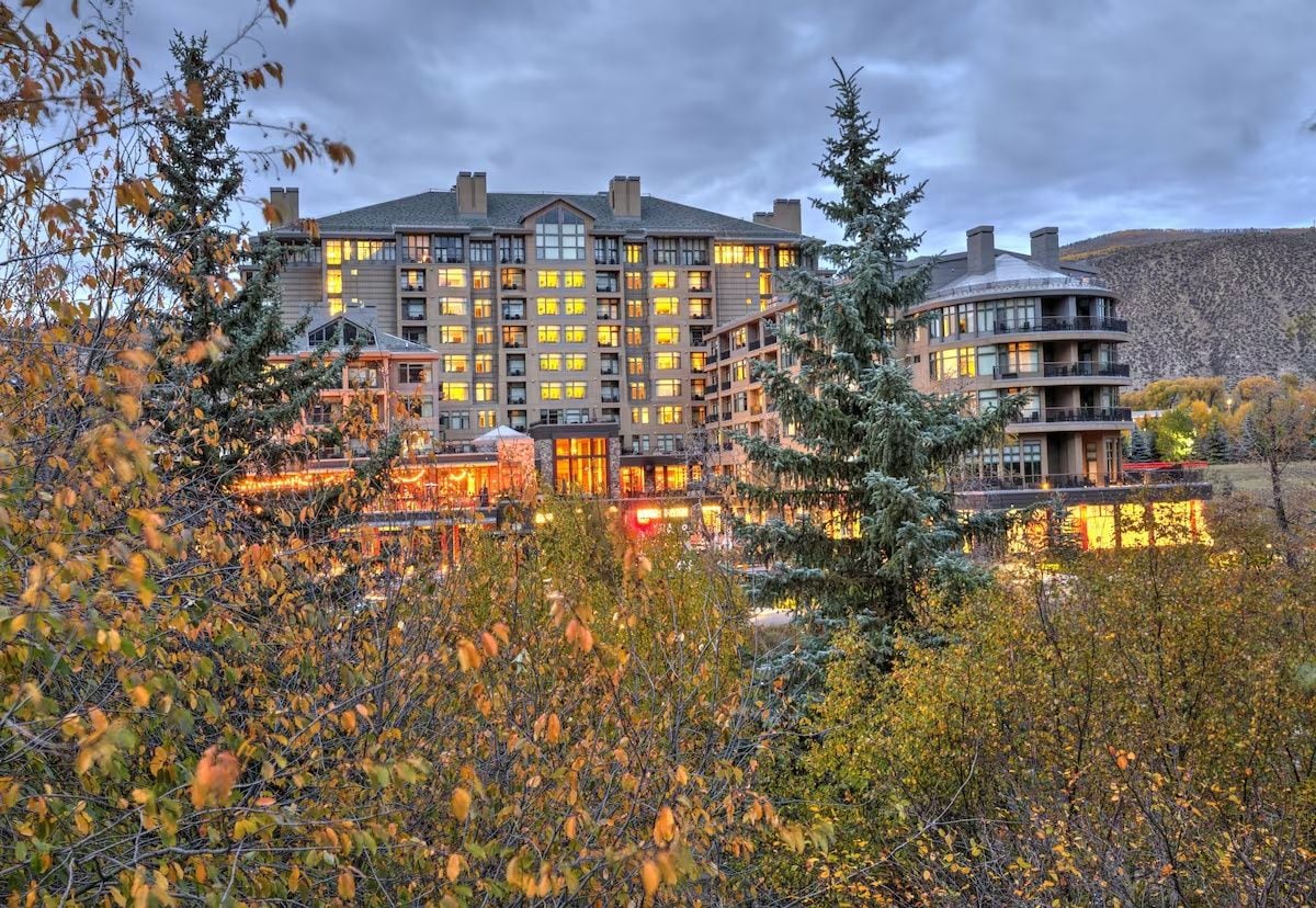 A multi-story hotel with a central courtyard, surrounded by trees and a mountainous backdrop.