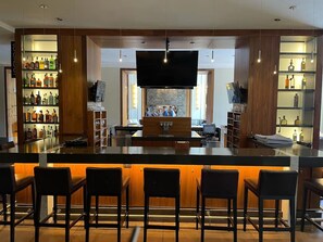 Eine Bar mit einer langen Theke, mehreren Barhocker und Regalen mit Flaschen.