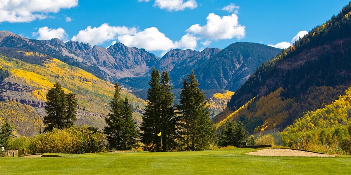 A golf course with a flag, trees, and mountains in the background.