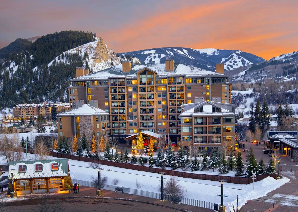 A multi-story hotel with a central atrium, surrounded by snow-covered trees and mountains.