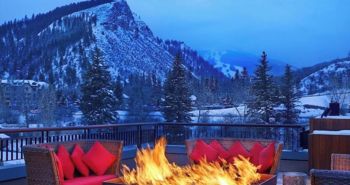 A balcony with a fire feature, wicker furniture, and a mountainous backdrop.