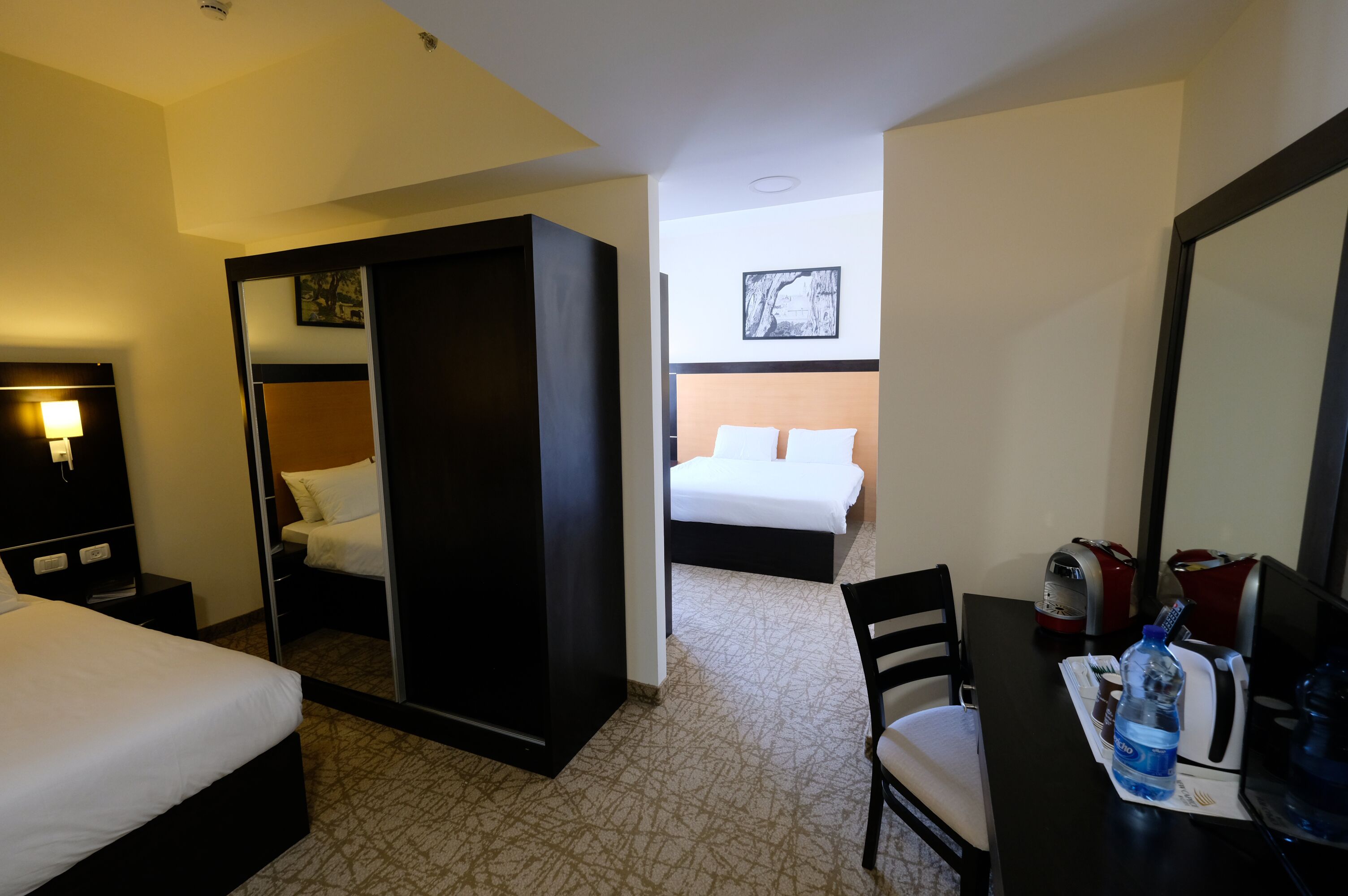A hotel room with two beds, a desk with a chair, a coffee maker, and a water dispenser.