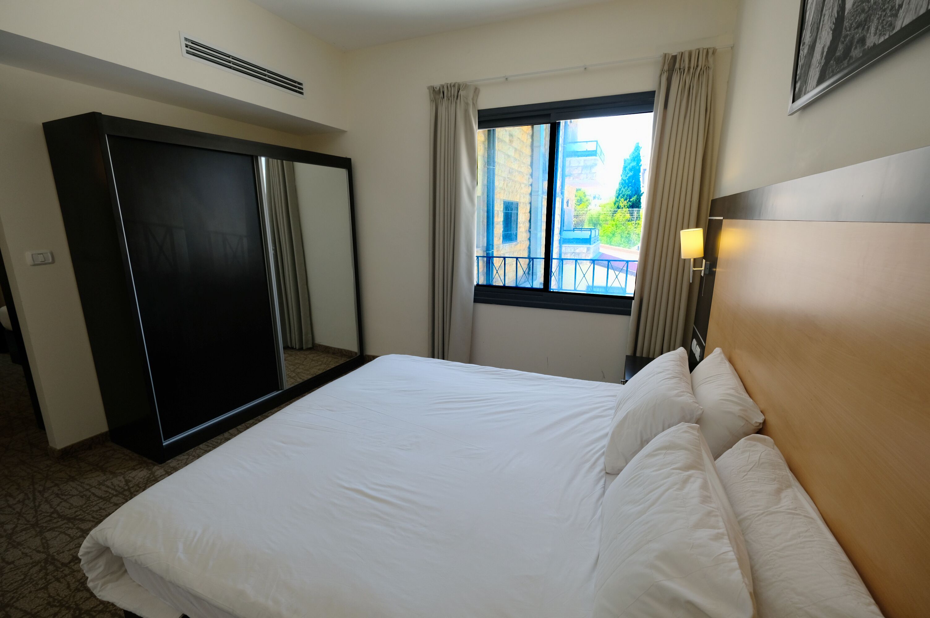 Een hotelkamer met een bed, een kledingkast, een raam met gordijnen en uitzicht op een gebouw.