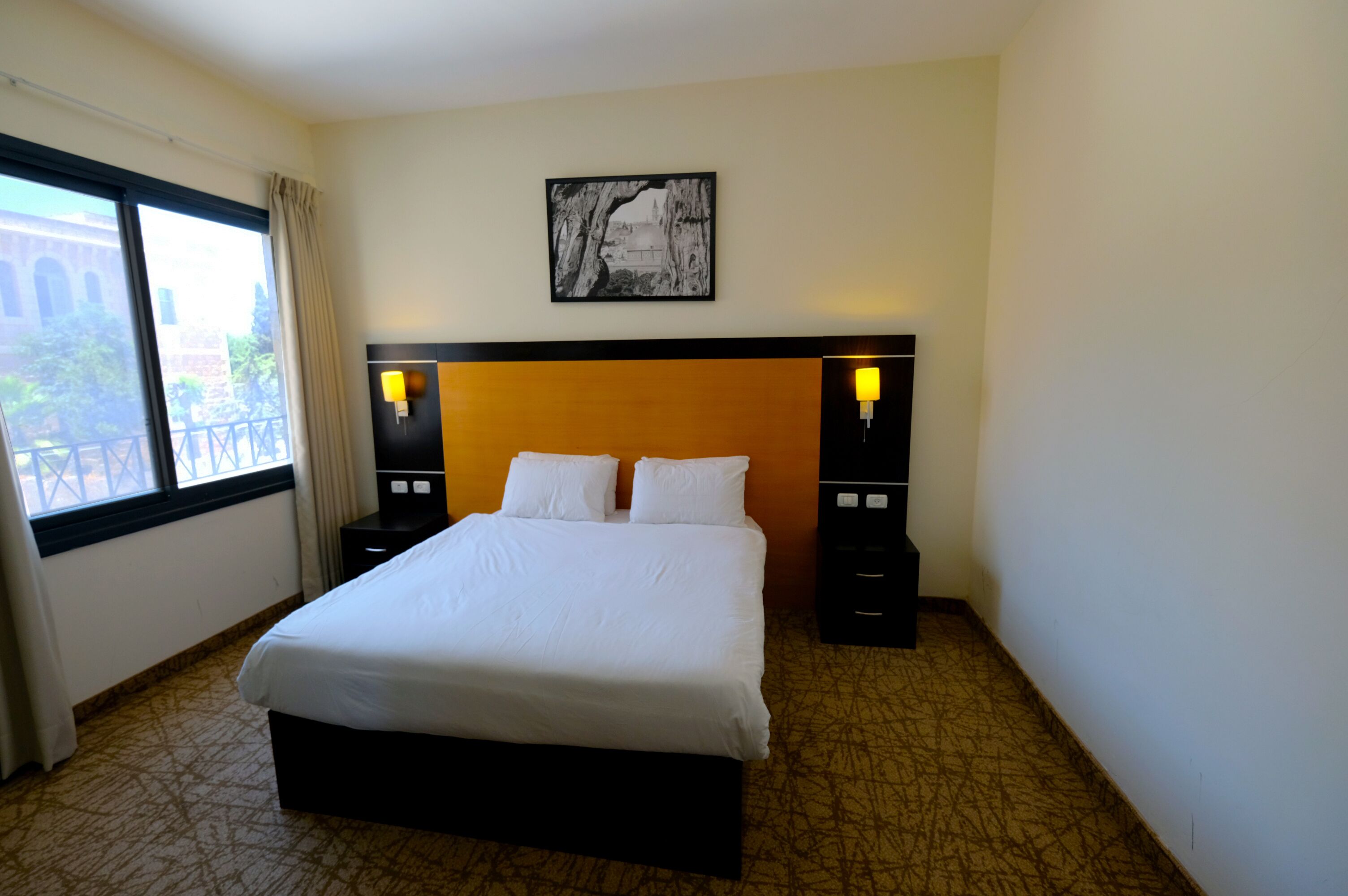 A hotel room with a large bed, two bedside tables with lamps, a framed picture on the wall, and a window with curtains.