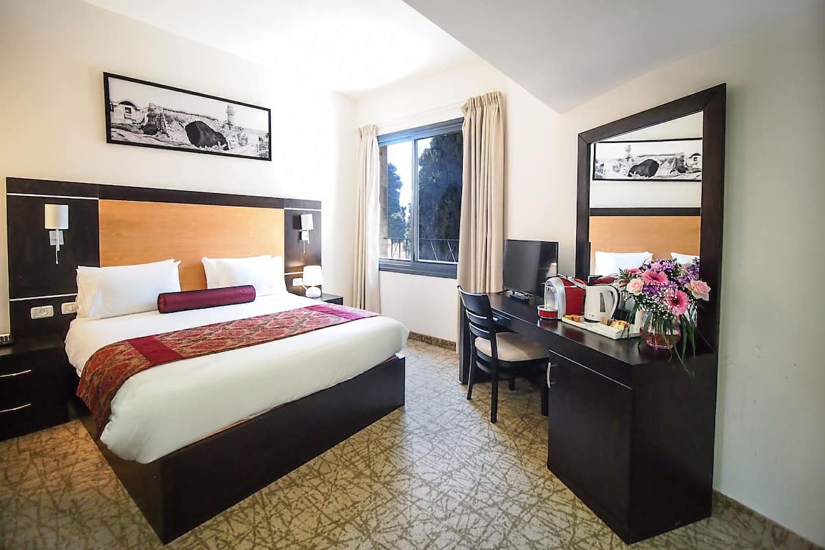 A hotel room with a bed, desk, chair, and a large window.