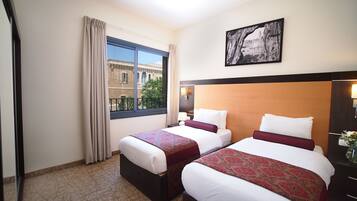 A hotel room with two beds, a large window with a view of a building, and a framed picture on the wall.