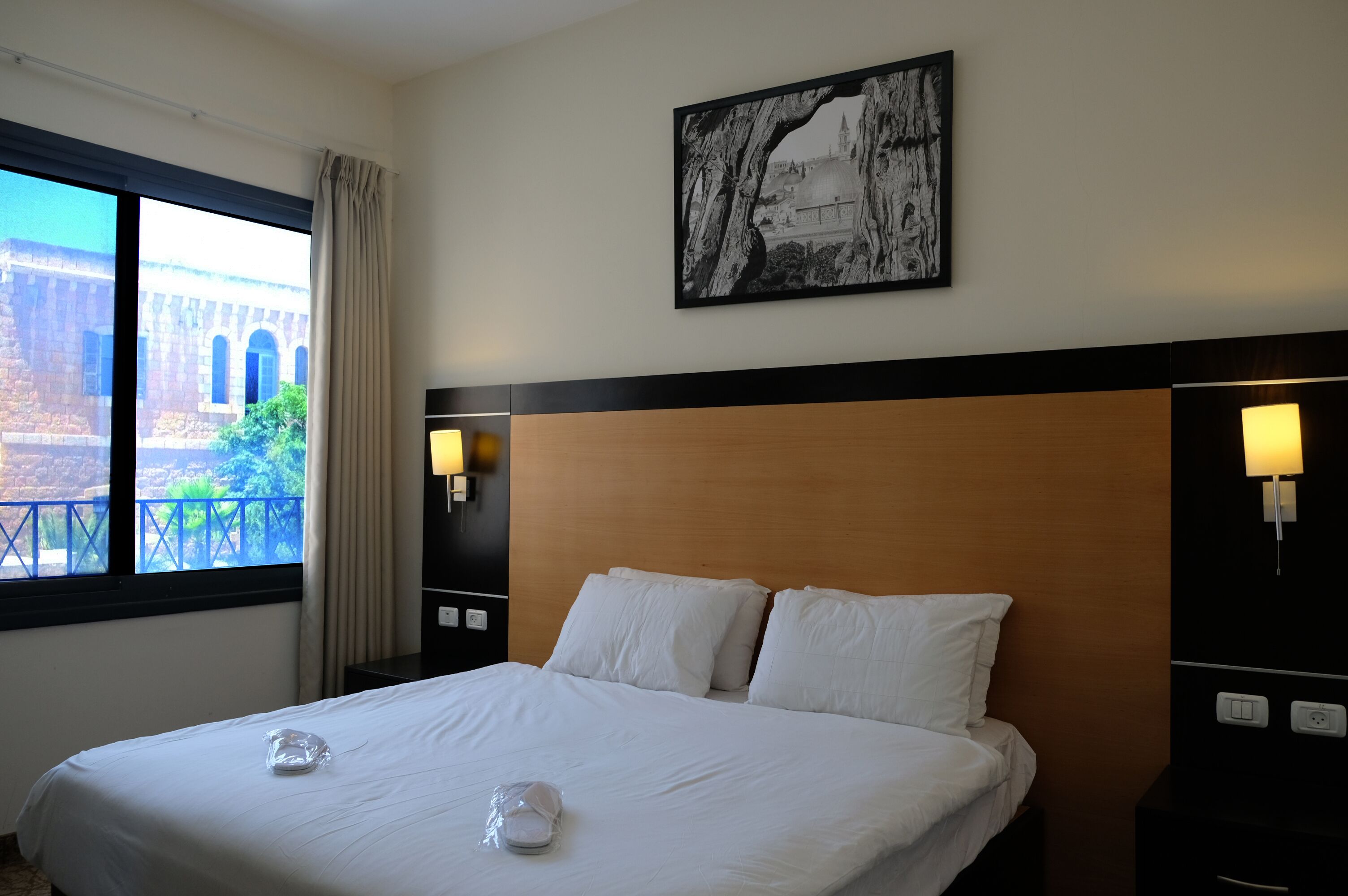 Habitación de hotel con una cama grande, vista de un edificio a través de la ventana y un cuadro en la pared.