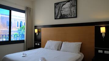 Habitación de hotel con una cama grande, vista de un edificio a través de la ventana y un cuadro en la pared.