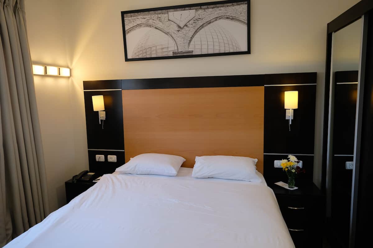 A hotel room with a large bed, two bedside lamps, a nightstand with a phone, and a framed picture on the wall.