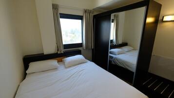 A hotel room with a large bed, a wardrobe, a window with curtains, and a mirror.