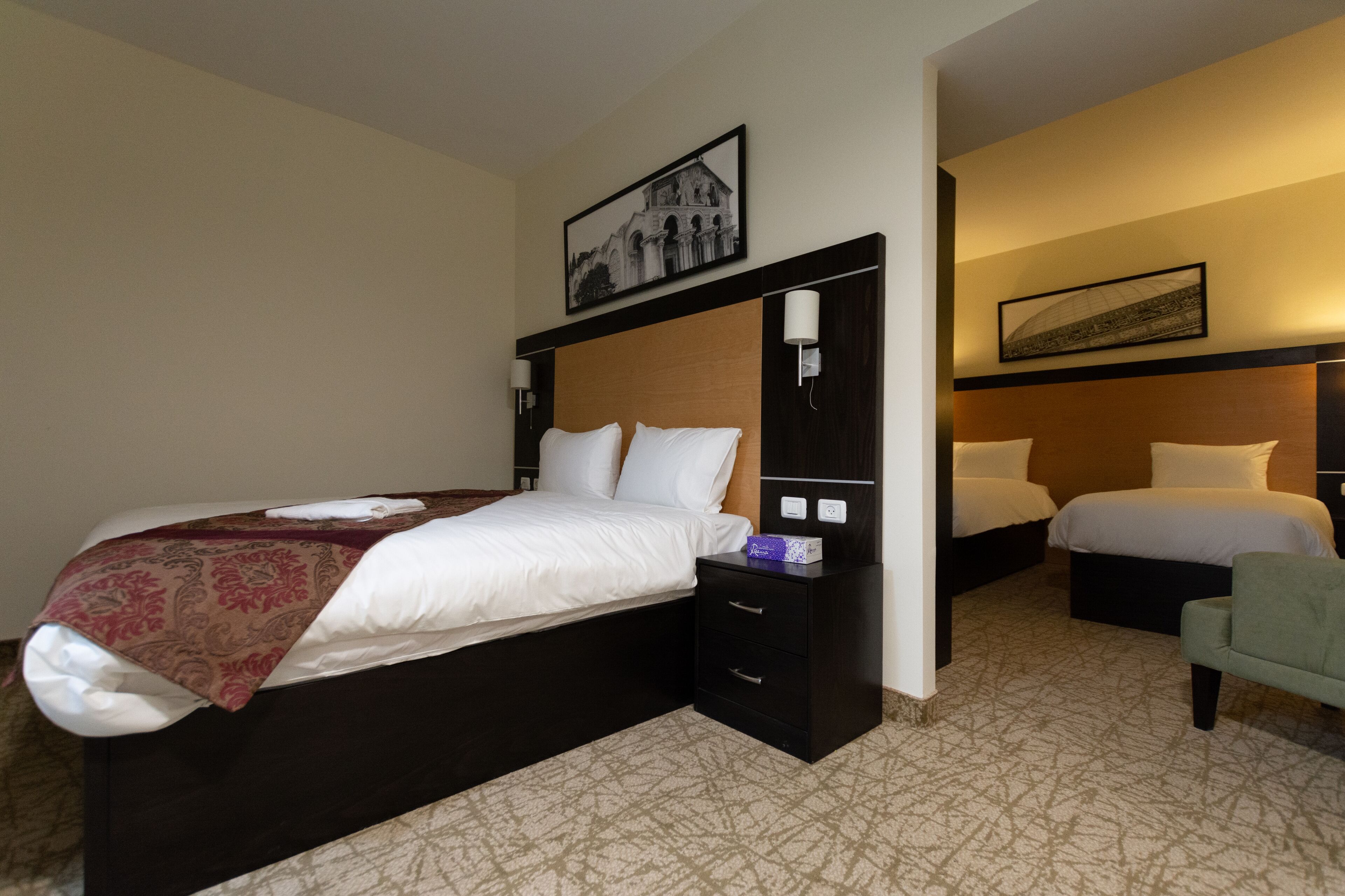 A hotel room with a large bed, a bedside table, a chair, and two smaller beds.