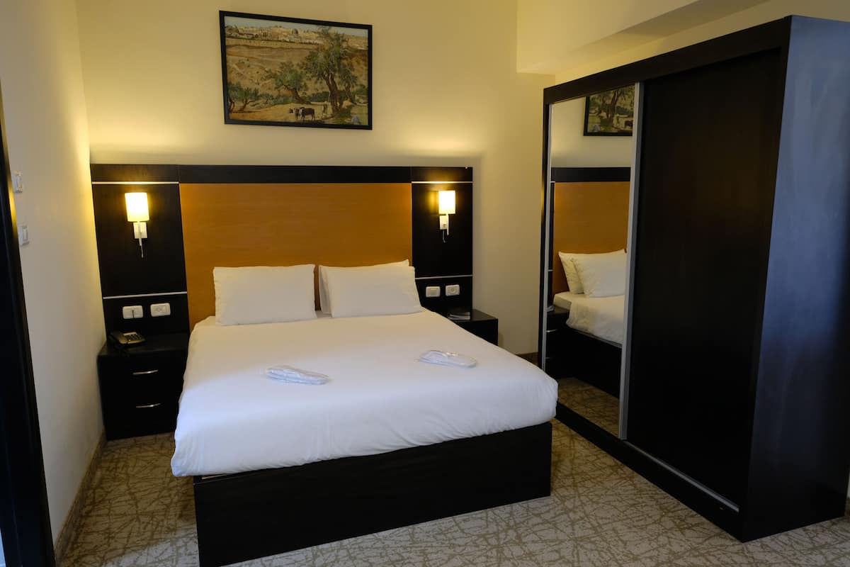A hotel room with a large bed, two bedside tables with lamps, a wardrobe, and a painting on the wall.