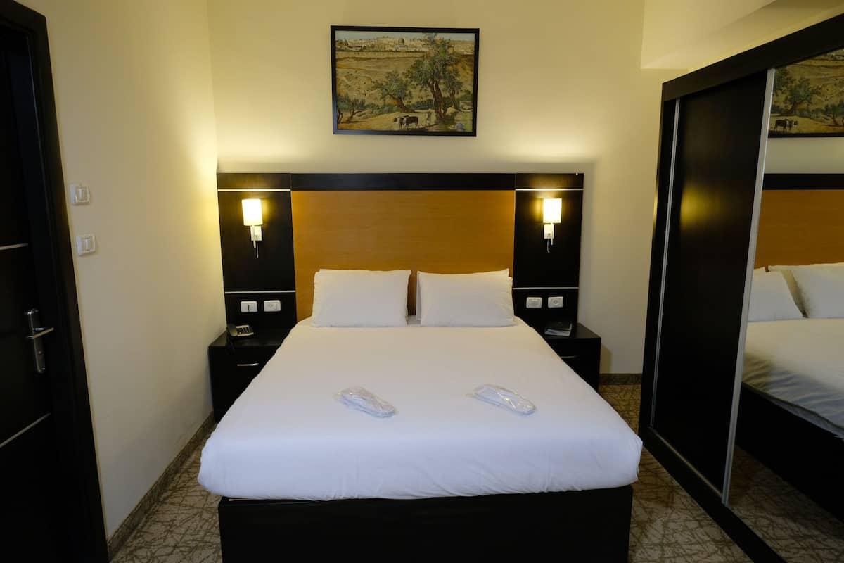 A hotel room with a large bed, two bedside tables, a nightstand, a mirror, and a painting on the wall.