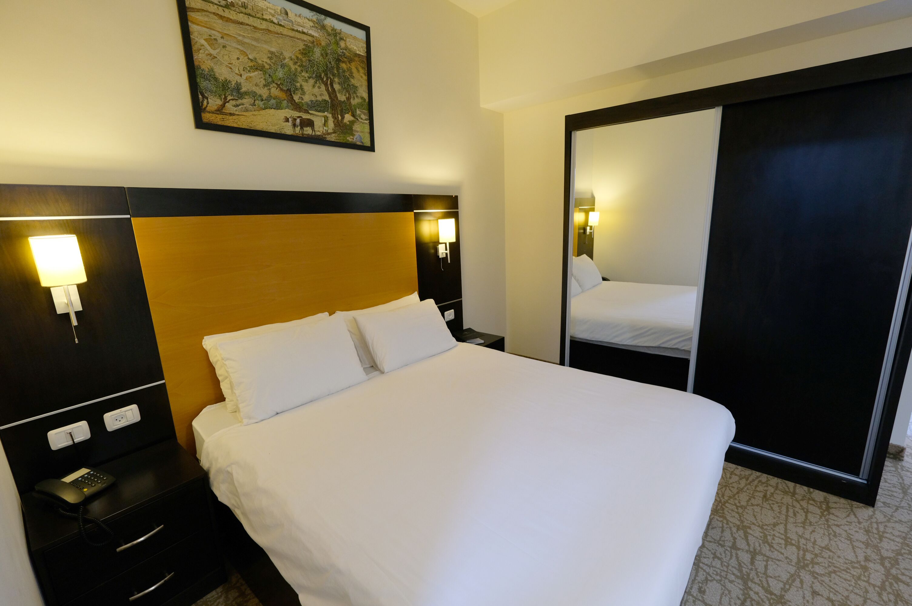 A hotel room with a large bed, bedside lamps, a nightstand with a phone, and a painting on the wall.
