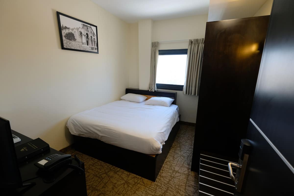 A hotel room with a bed, a desk with a telephone, a framed picture on the wall, and a window with curtains.
